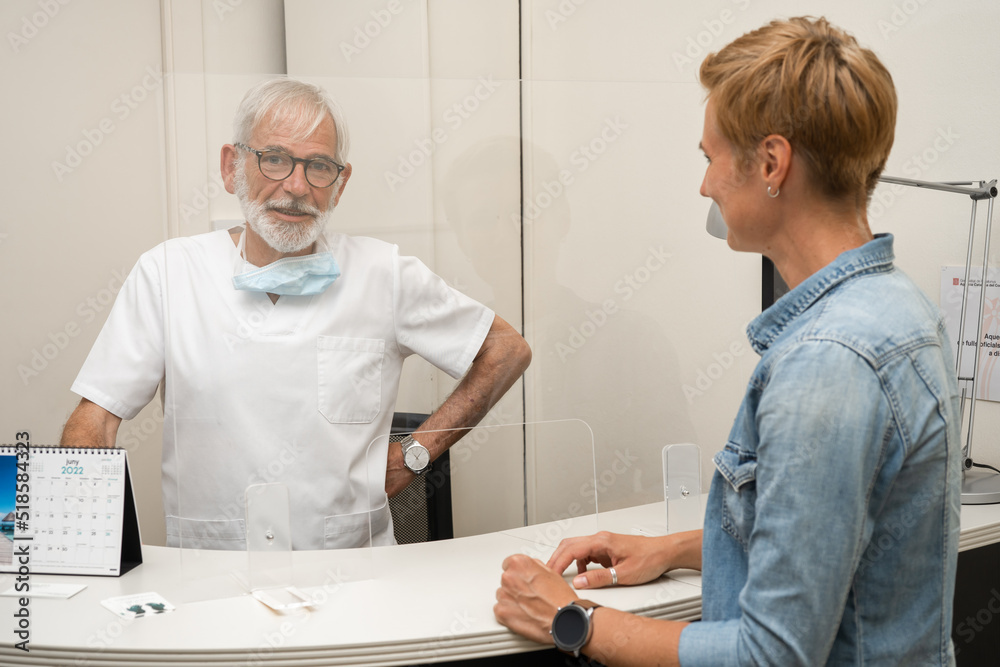 Obraz premium Settlement of the patient at the registrar in medical clinic after examination by a doctor or dentist. Mature male doctor with grey hair and beard, and female patient.