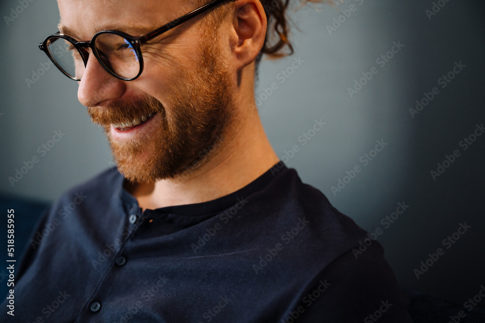 Young ginger man wearing eyeglasses smiling while resting on sofa Young ginger man wearing eyeglasses smiling while resting on sofa