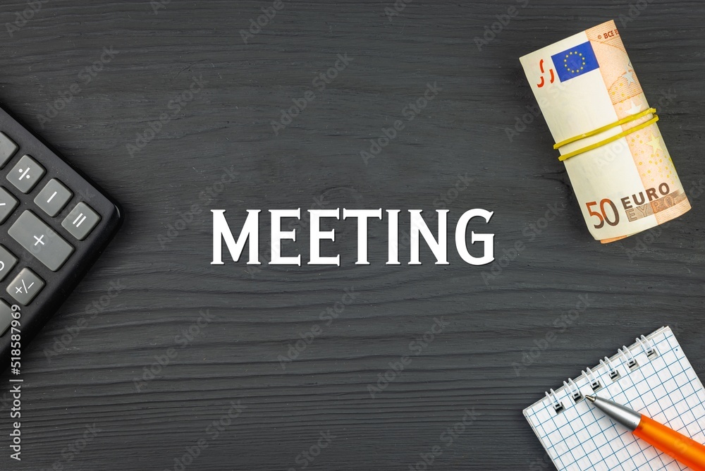 MEETING - word (text) and euro money on a wooden background, calculator, pen and notepad. Business concept (copy space).