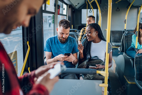 Fotografiet Multiracial friends talking and using a smartphone while riding a bus in the cit