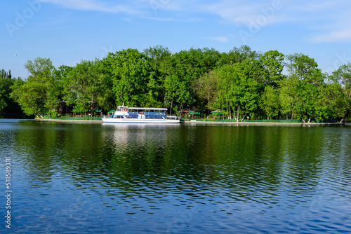Landscape with white boats on Herastrau lake and large green trees in King Michael I Park (former Herastrau) in Bucharest, Romania, in a sunny autumn day.