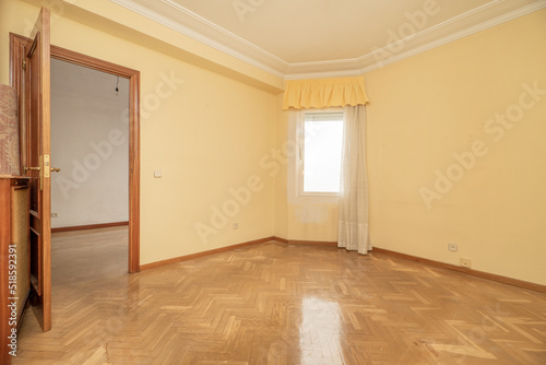 Empty room with shiny oak hardwood floor  matching woodwork  cream walls and curtained window