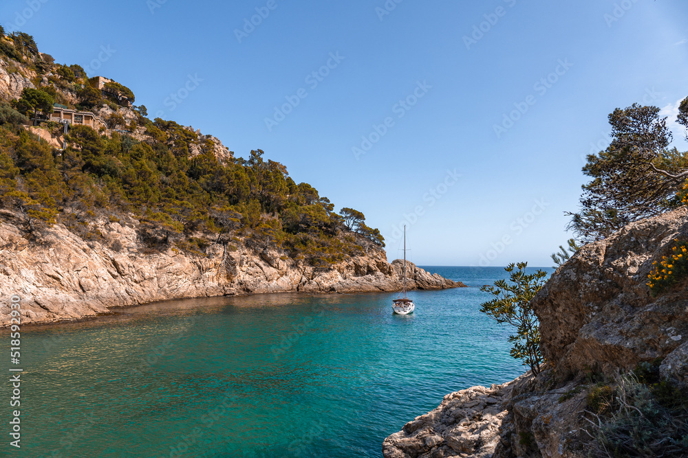 Coastal landscape with rocky hills and trees. Boat or yacht sailing on the shore on Costa Brava in Spain