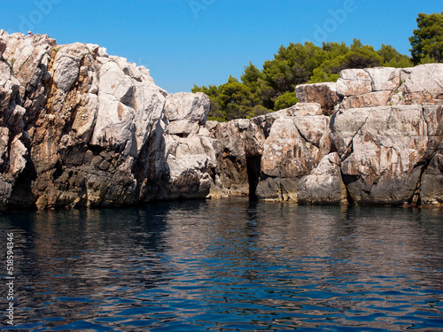 Beautiful view of the rocky coast of the island with a forest and blue sky in the background, a view from the sea