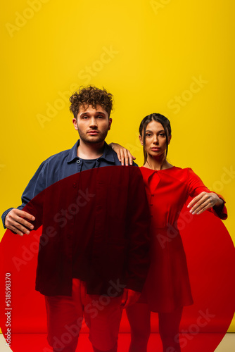 trendy woman and man holding round shape glass while posing isolated on yellow.