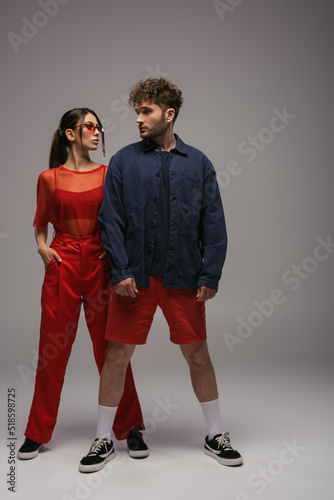 full length of stylish man and woman in trendy outfits posing on grey.