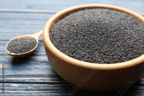 Poppy seeds in bowl on blue wooden table, closeup