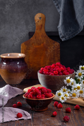 Fresh raspberries in a clay and wooden bowl on a dark wooden table