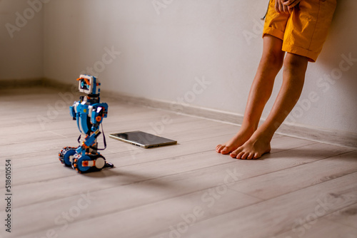 Kid stand alone with robot from plastics details. tablet lie on floor near boy. concept of loneliness among teenagers photo