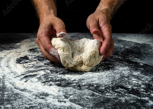 Hands knead the dough for further preparation, dark background.