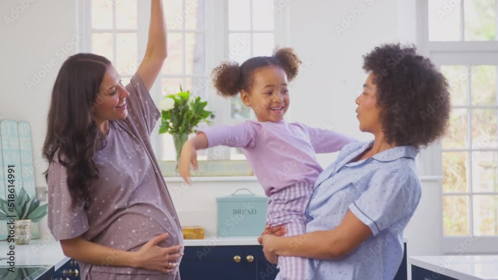 Pregnant family with two Mums wearing pyjamas making morning pancakes in kitchen and dancing with daughter - shot in slow motion