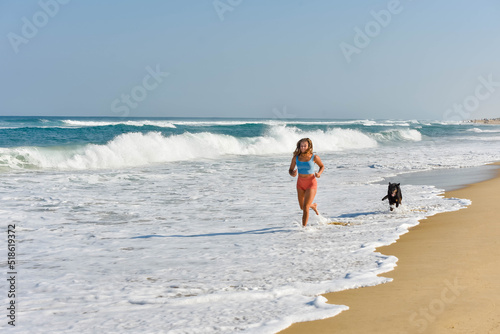 Attractive athletic young woman in shorts and top running with her dog on the sunny beach