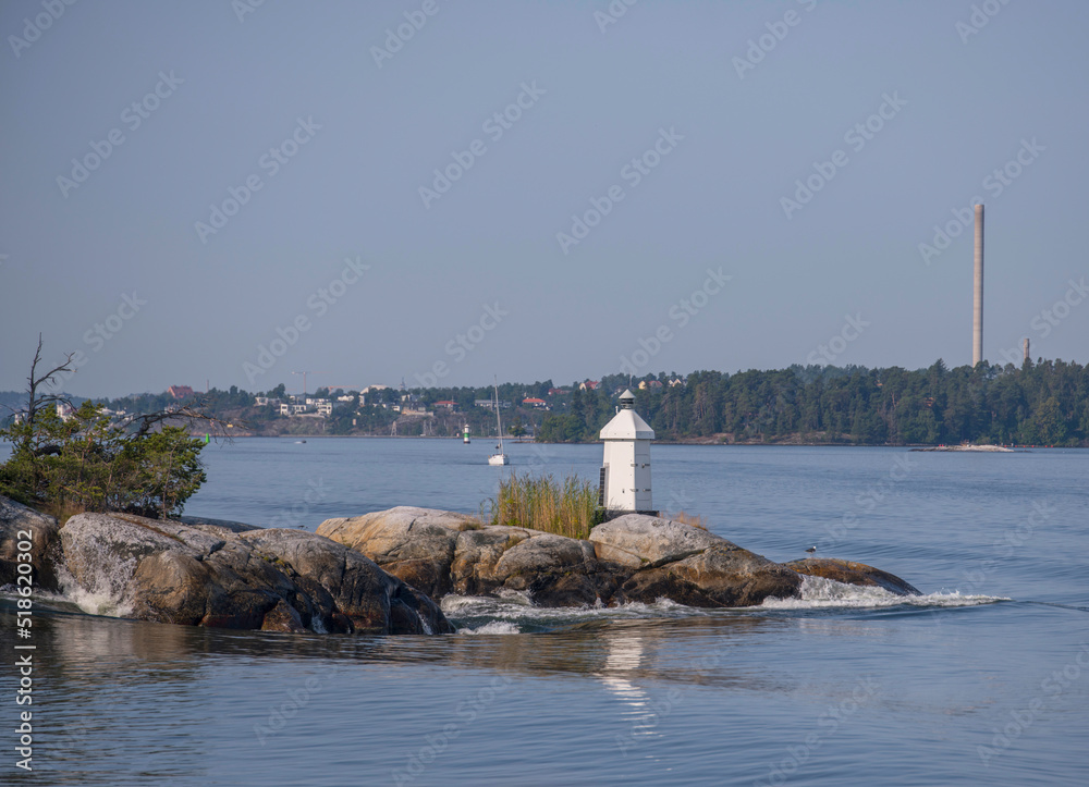 Small light house on a cliff, wave surge from a boat a sunny summer day in Stockholm