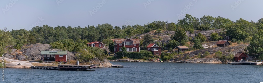 Panorama view, commuting boat jetty, island Södra Stavsudda, summer houses on smooth cliffs, jetties and boats at an open bay in the archipelago a sunny summer day in Stockholm
