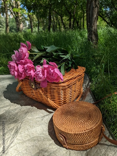 Wooden basket and bag with flowers on summer picnic with green grass on background.