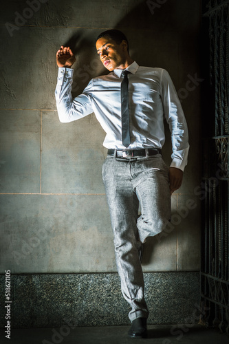 Obraz na płótnie Against the Wall. Young black businessman wearing white shirt, gray pants, leather shoes, black tie, standing outside metal gate, against the wall, into deeply thinking.. w salonie
