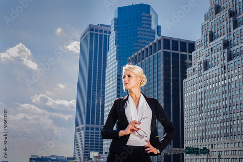 Obraz na płótnie Inspiration. Young blonde businesswoman wearing white underclothes, black suit unbuttoned, holding glasses, standing in front of business district in New York City, hopefully looking forward. w salonie
