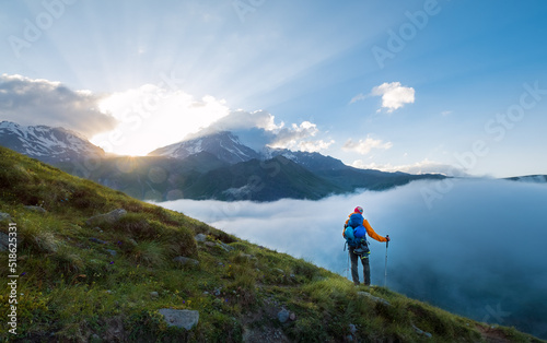 Photo Lonely mountaineer descending from Kazbek 5054m mountain with backpack, helmets high mountaineering boots and trekking poles standing and enjoying sunset after successful ascending, Caucasus, Georgia
