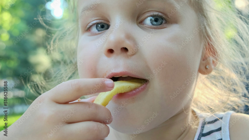 Little girl eat french fries. Close-up of blonde girl takes potato chips with her hands and tries them sitting in street cafe on the park. Little girl eat french fries. Close-up of blonde girl takes potato chips with her hands and tries them sitting in street cafe on the park.