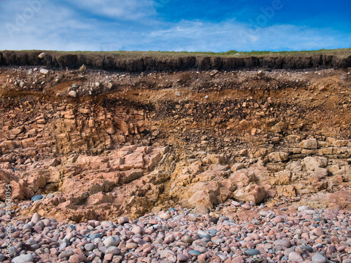 Eroding soil, subsoil and bedrock at a pebble beach near Sand Wick and Hillswick in Northmavine, Shetland, UK. Taken on a sunny day with a blue sky in the background. photo