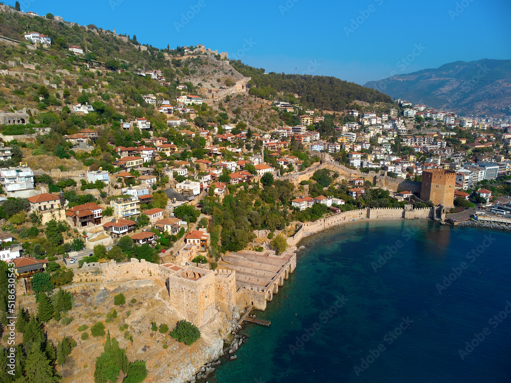 panoramic view on a fence made of brick fortress and the city of Alanya in Turkey, many small houses from afar, around green trees