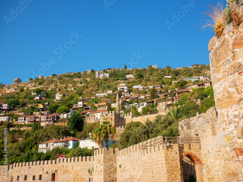 panoramic view on a fence made of brick fortress and the city of Alanya in Turkey, many small houses from afar, around green trees photo