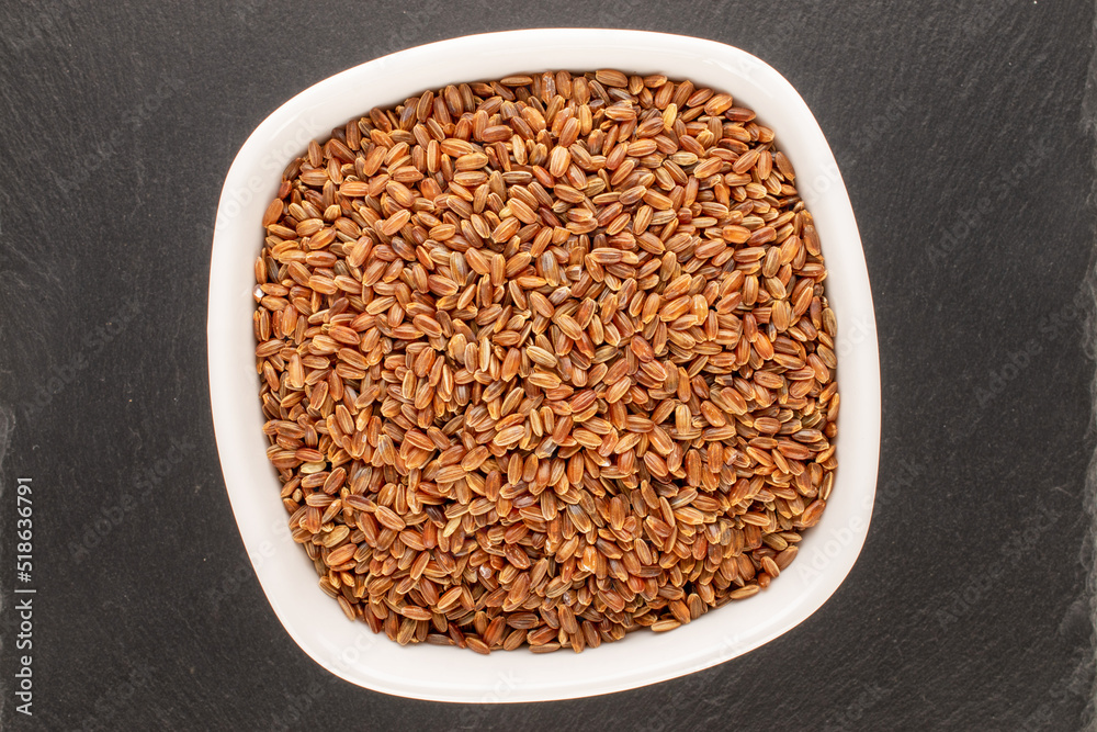 Organic uncooked brown rice in a ceramic plate on a slate stone, close-up, top view. Organic uncooked brown rice in a ceramic plate on a slate stone, close-up, top view.