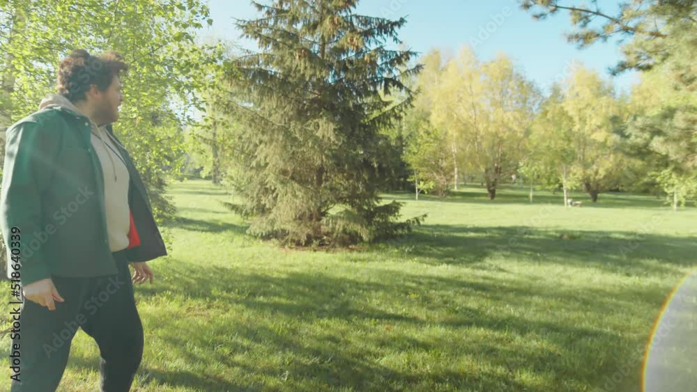 Man throwing ring toy as his staffordshire terrier dog chasing it and bringing back while playing fetch in park on sunny day