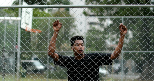 Pensive young black man leaning on metal fence. Contemplative mixed race person