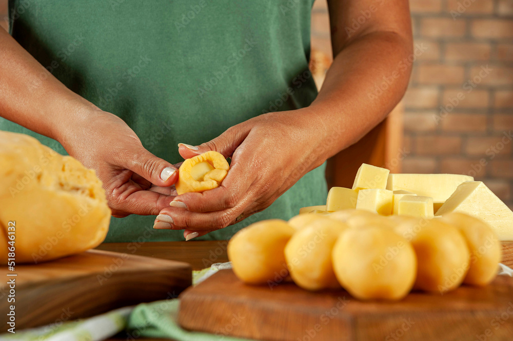Woman preparing brazilian cheese stuffed croquette (bolinha de queijo) on a wooden table.
