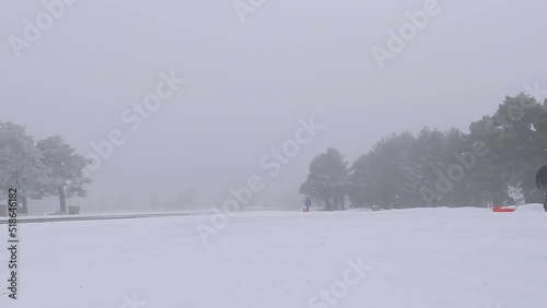 Boy with a sled going up a toboggan run under an snow storm