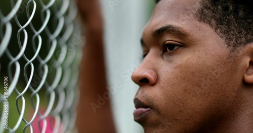 Pensive angry young black man leaning on metal fence outside thinking