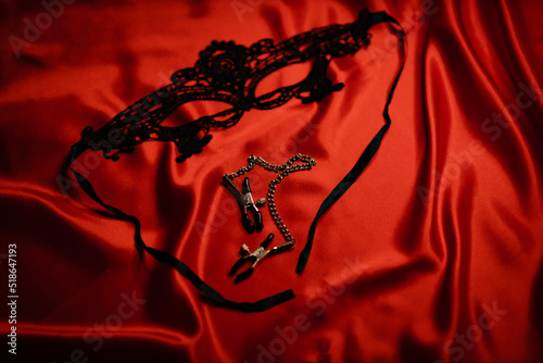 Black mask and nipple clamps on a red background. Love games. Games for adults. soft focus