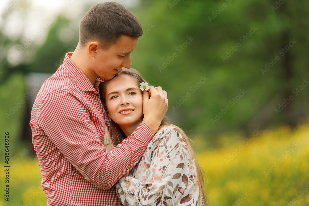 Young loving couple gently hugging, a lot of yellow flowers are around on the field. Enjoying time together. Man puts chamomile in woman's hair. Young loving couple gently hugging, a lot of yellow flowers are around on the field. Enjoying time together. Man puts chamomile in woman's hair.