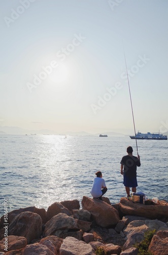 Fotografie Vertical shot of two men trying to catch fish with a fishing nod in Hong Kong