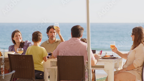 Family and friends gathered for lunch enjoying a delicious paella in a bar on the beach - happy little kids playing around the table after eating, eating dessert and ice cream © Quality Stock Video