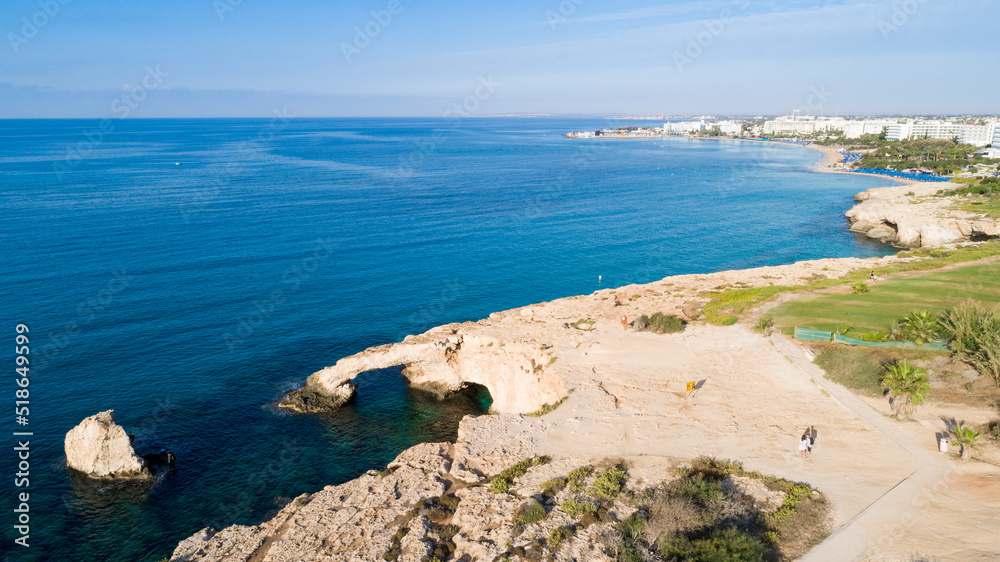 Aerial bird's eye view of coastline landmark ‘Love bridge’ and sea caves at Cavo Greco, Ayia Napa, Famagusta, Cyprus from above. A tourist attraction cliff rock natural formation arch in Ammochostos.