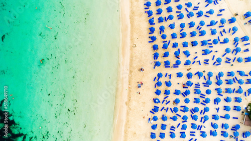 Aerial bird's eye view of Makronissos organised beach coastline, Ayia Napa, Famagusta, Cyprus from above. Blue aligned umbrellas, golden sand, parasols, people sunbathing sun beds clean turquoise sea. photo