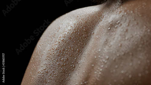 Big close-up shot of young good-looking slim African American female model's wet shoulders on black background | Clean body concept