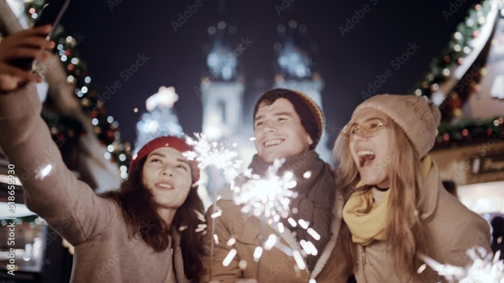 Happy young multiracial friends asian girl use a smartphone communicating, podcast video chat Europe night street. Woman looking at phone selfy with falling sparkling glowing sparklers fireworks light Happy young multiracial friends asian girl use a smartphone communicating, podcast video chat Europe night street. Woman looking at phone selfy with falling sparkling glowing sparklers fireworks light