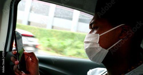 Black man in taxi browsing internet on smartphone device wearing pandemic mask
