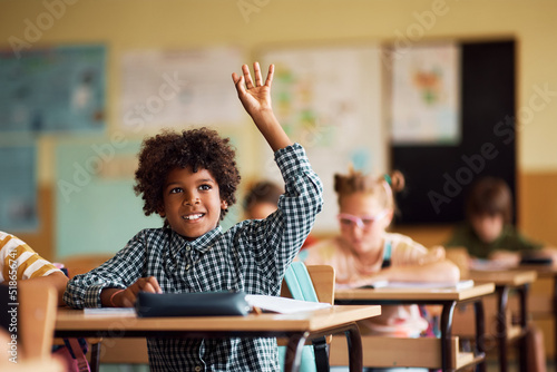 Fotografija Happy African American kid raising his arm to ask question during class at elementary school