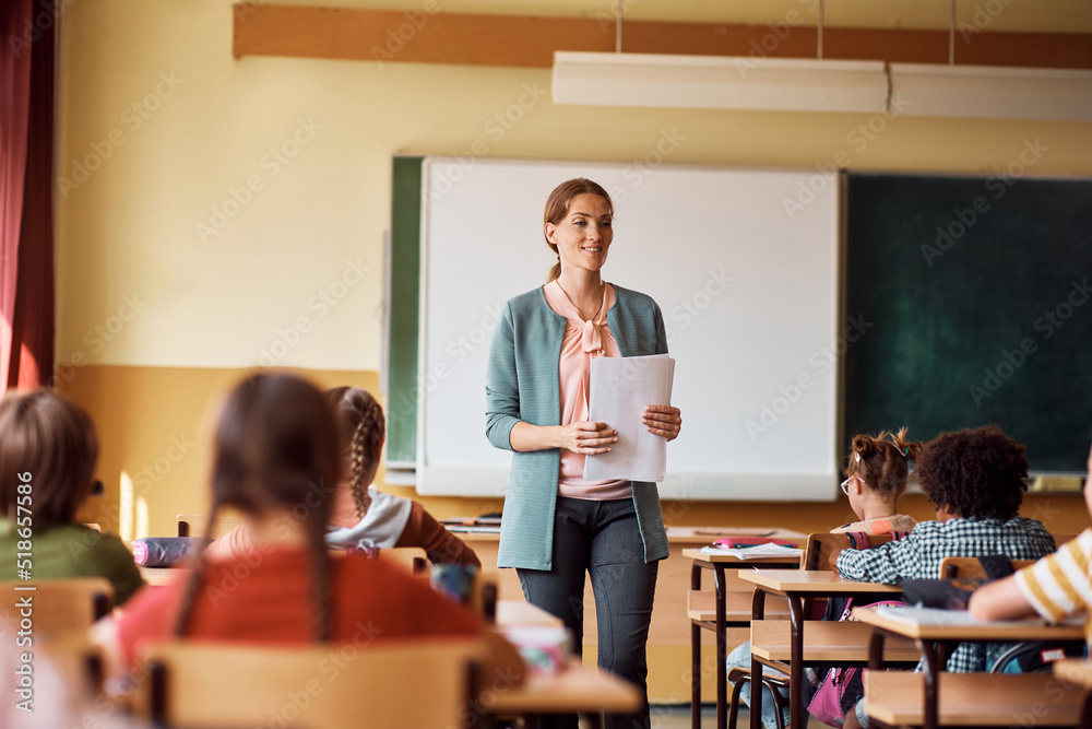 Happy elementary school teacher giving lecture to her students in classroom. Happy elementary school teacher giving lecture to her students in classroom.