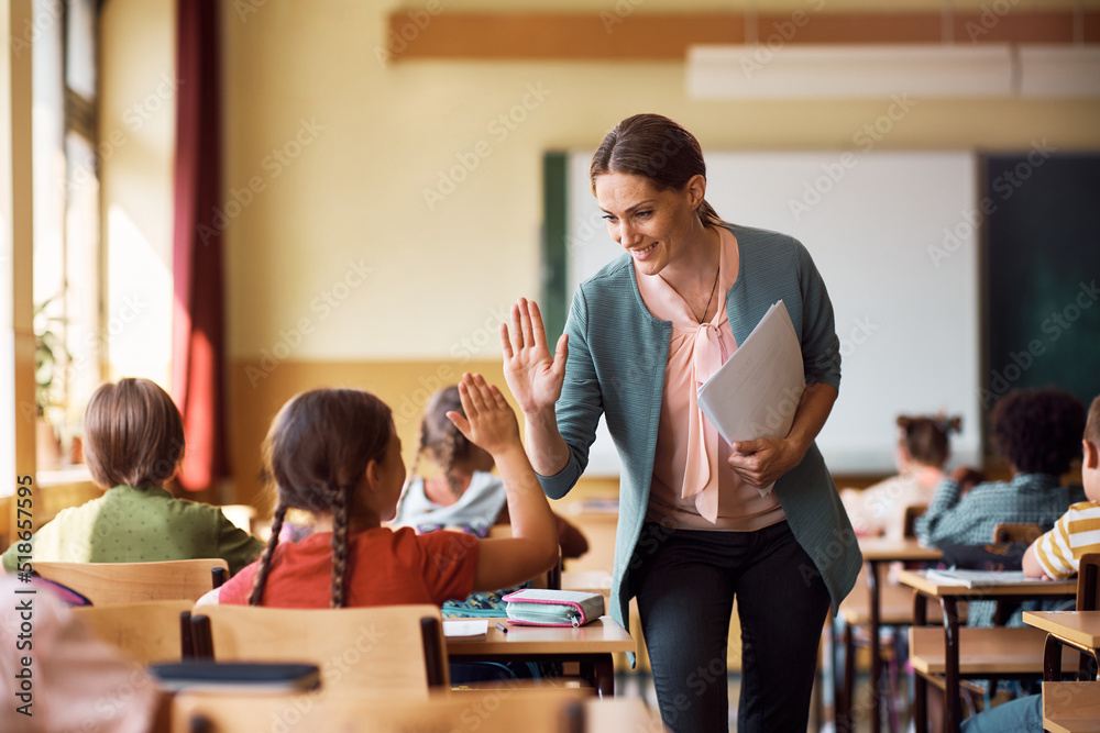 Happy teacher and schoolgirl giving high five during class at school. - obrazy, fototapety, plakaty 