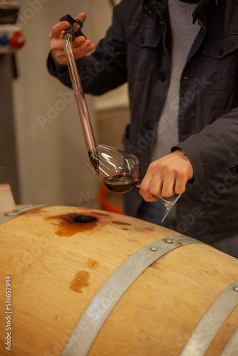 man making a sample of red wine from barrel with a special tool