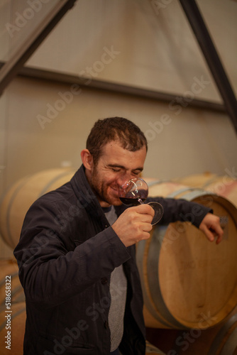 man tastes red wine from the glass near wooden barrel at the winery
