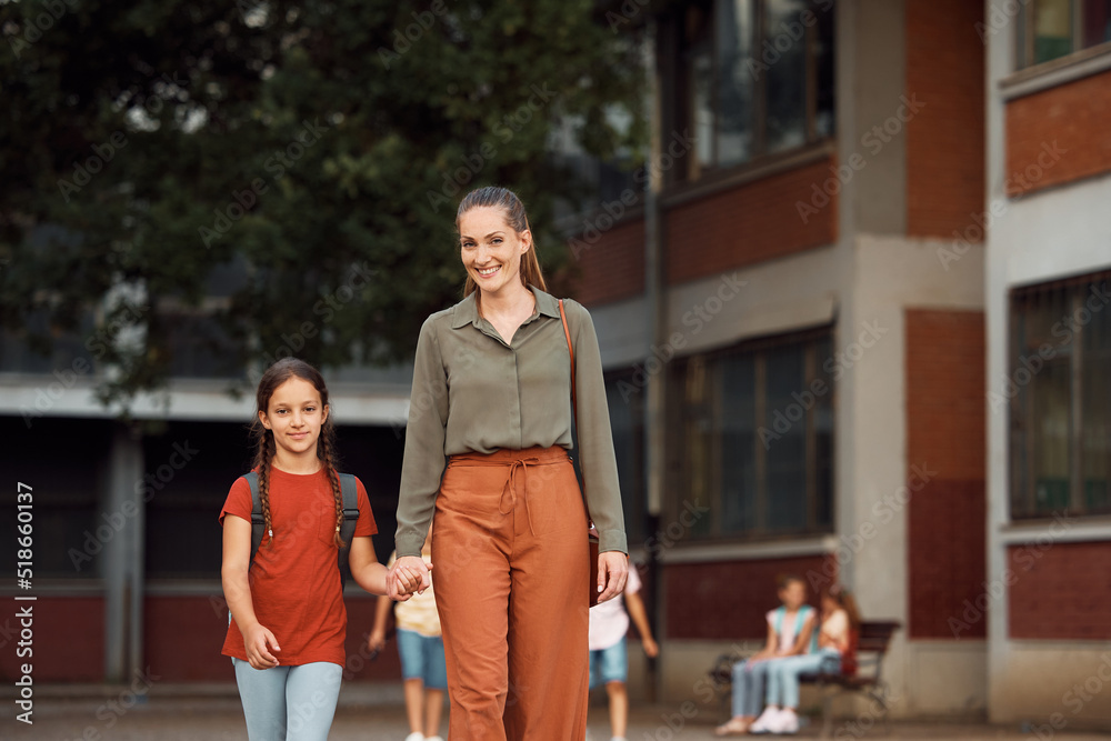 Happy mother and daughter walking in schoolyard and looking at camera.