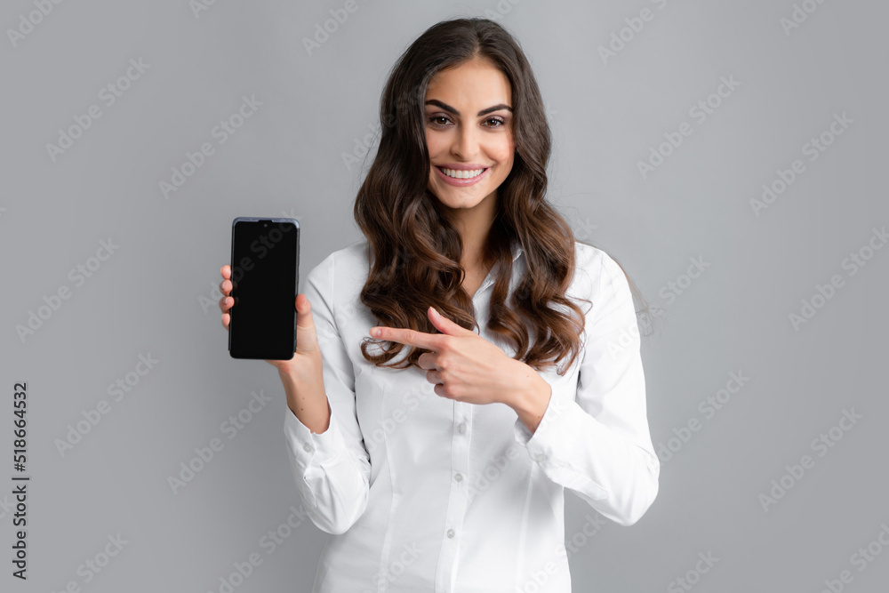 Happy young woman showing empty smartphone screen. Smiling young brunette business woman girl in shirt isolated on gray background, studio portait. Beauty girl using mobile phone, typing sms message. Happy young woman showing empty smartphone screen. Smiling young brunette business woman girl in shirt isolated on gray background, studio portait. Beauty girl using mobile phone, typing sms message.