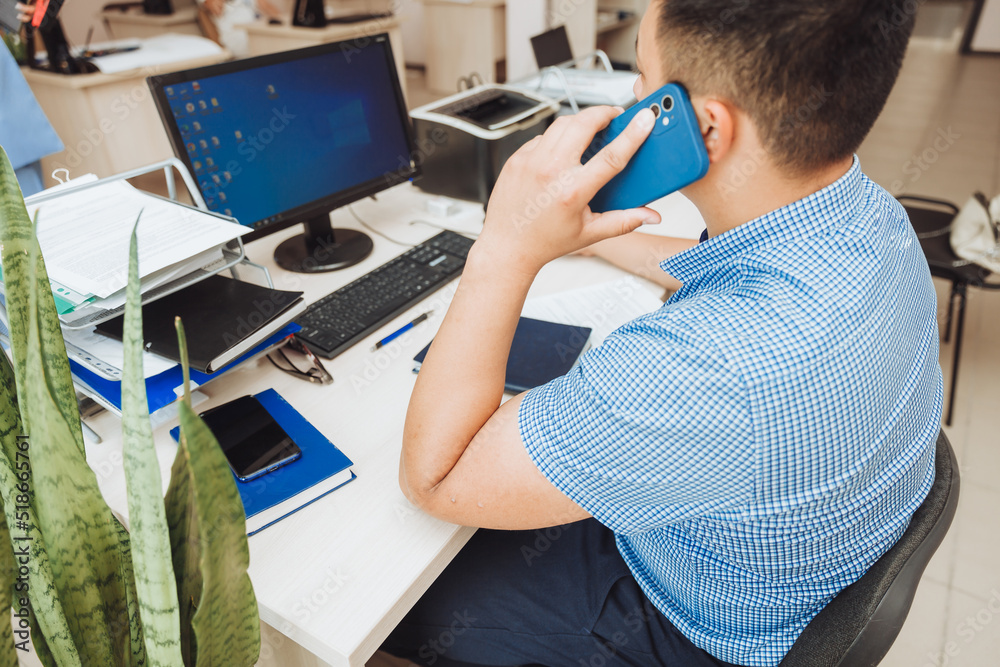 a young Asian businessman is talking on the phone to discuss work in the office. the man is Asian. a young Asian businessman is talking on the phone to discuss work in the office. the man is Asian.