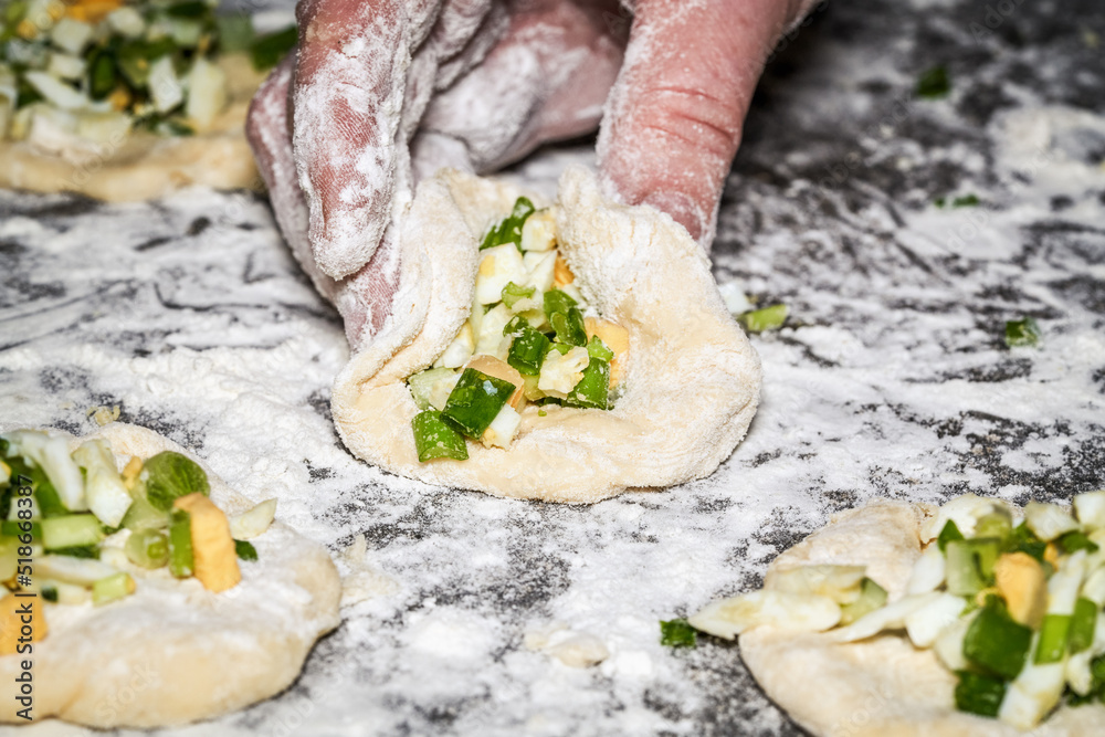 Womens hands mold pies stuffed with onions, eggs and greens
